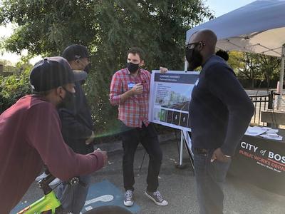 Two men hold a board while two others stand in front of them. They are talking about changes to Cummins Highway