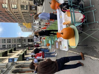 Tables, easels, and chairs are set up in the parking lane on State Street. People are looking at materials and walking on the sidewalk.