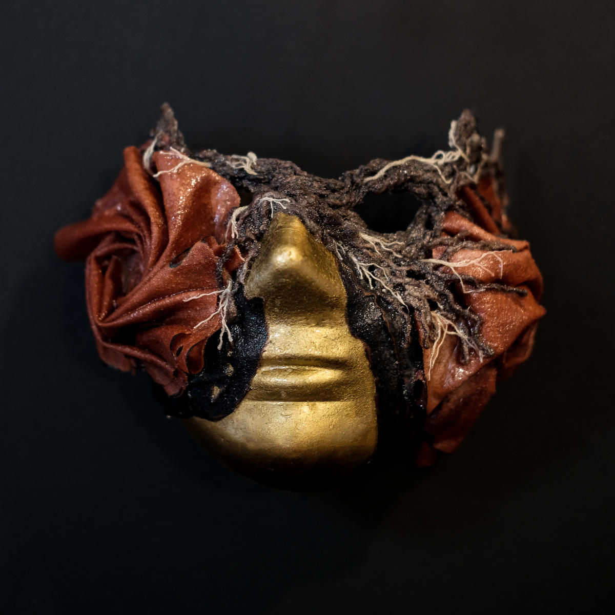 3D artwork, a masquerade mask made of gold material and red fabric manipulated into swirling, folding shapes