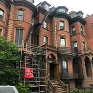 View of the front façade of an ornate 1850s South End brownstone building with scaffolding on the outside